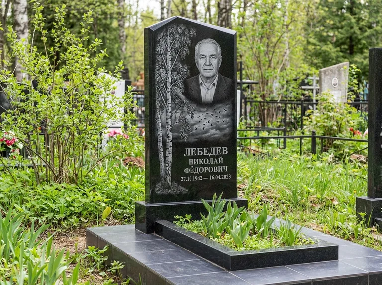 Памятник с гравировкой берёзы: вертикальная стела со скошенным верхом — берёза и стая птиц в небе, гранитный цоколь с тёмной плиткой, работа «Лебедев» в Мурманске
