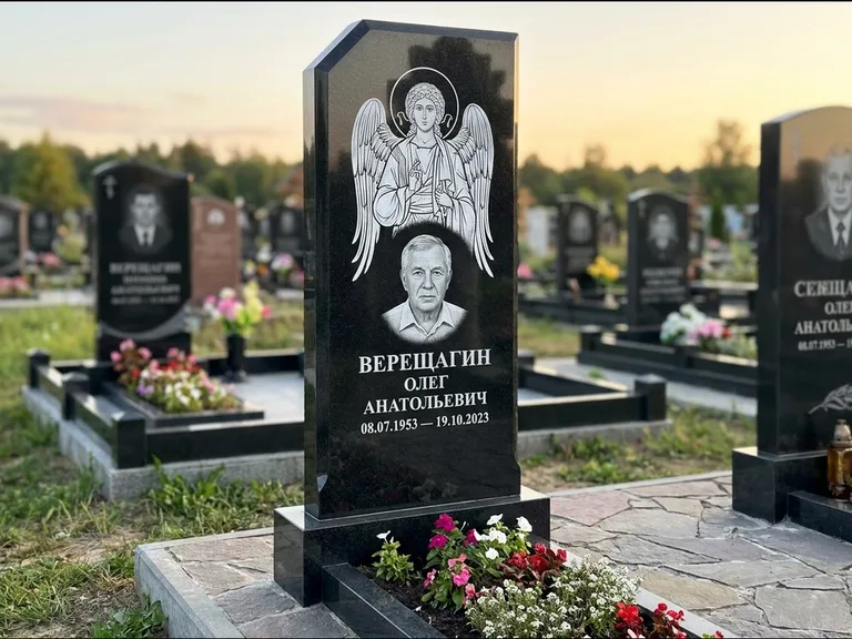 Памятник с гравировкой иконы: стела с резным навершием и нимбом в золоте — гравировка образа Спасителя, высокие разросшиеся туи полукругом, работа «Мельникова» в Мурманске