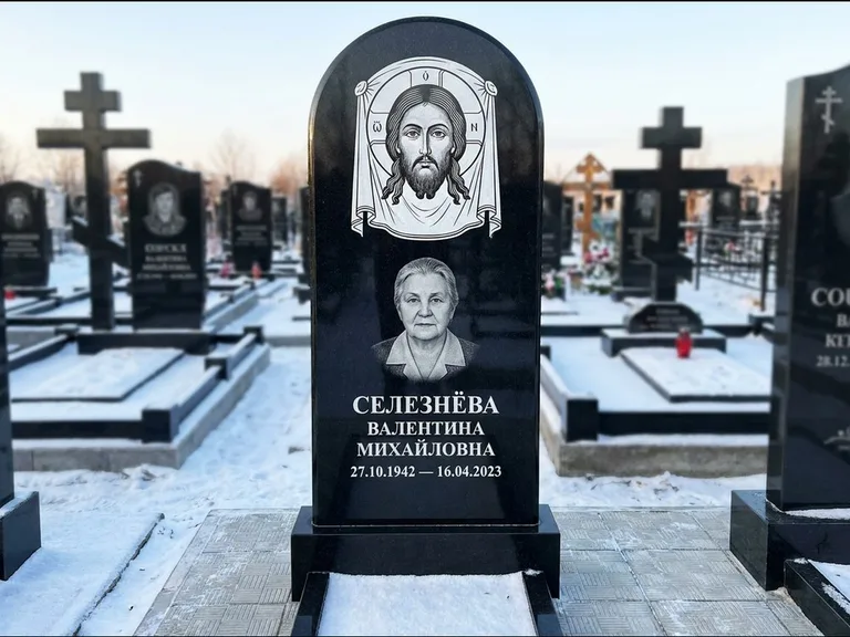 Памятник с гравировкой иконы: небольшая скромная одиночная стела с именной иконой — золочёный нимб на образе, аккуратный участок с газоном, работа «Ковалёв» в Мурманске