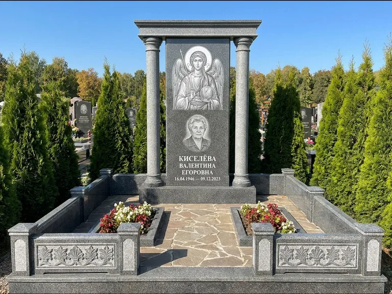 Памятник с гравировкой иконы: массивная стела с двускатным навершием-домиком — гравировка Николая Чудотворца, живая изгородь из туи, работа «Журавлёв» в Мурманске