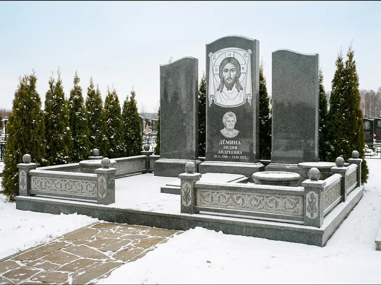 Памятник с гравировкой иконы: узкая вертикальная стела-пилон с ликом — икона в резной рамке-киоте, открытая лужайка без ограды, работа «Одинцов» в Мурманске