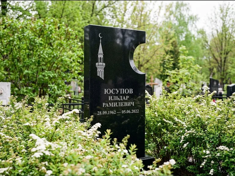 Мусульманский памятник с гравировкой мечети: стела с боковым вырезом в форме полумесяца — гравировка минарета с полумесяцем, низкие кусты спиреи в цвету, работа «Юсупов» в Мурманске