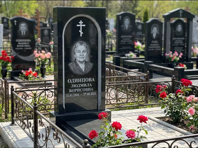 Памятник из чёрного гранита — скромная невысокая стела с крестом с терновым венцом, работа «Лаврентьева» в Мурманске
